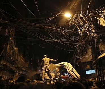 A man directs a bulldozer as he stands under a cluster of overhead wires at the site of the collapsed building
