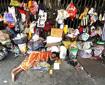 A woman sleeps in front of her belongings, hanging from the shutters of a shop, in Kolkata