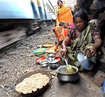 A woman cooks using a makeshift stove in a slum as a train passes by in Dhaka