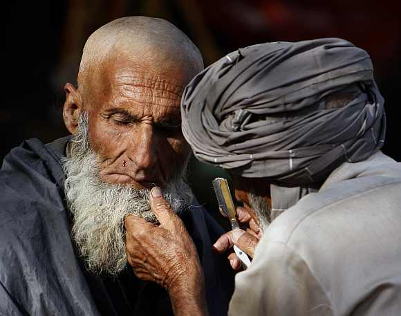 A street barber nicks the face of a man as he gives him a shave in Kabul