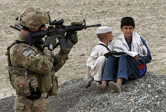 Afghan residents sit on the ground near a US army soldier securing the perimeter of a government building in Laghman province