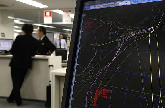 Japan Airlines pilots look at a monitor next to a computer screen showing no-fly zones in red, as well as a new route that would avoid an accident with North Korea's planned long-range rocket launch in a Japan Airlines' pilot ready room at Haneda airport in Tokyo