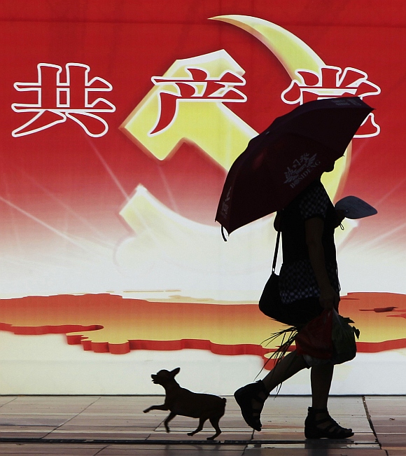 A woman and a pet dog walk past a poster depicting the logo of the Communist Party of China in Chongqing municipality