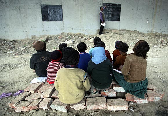 Children sit on bricks as they attend their class in an open charitable school