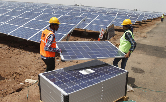Workers carry photovoltaic solar panels for installation at the Gujarat solar park