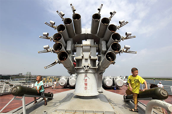 Children play next to a rocket launcher on the decommissioned former Soviet aircraft carrier Kiev at Bagua beach, on the outskirts of northern China's Tianjin