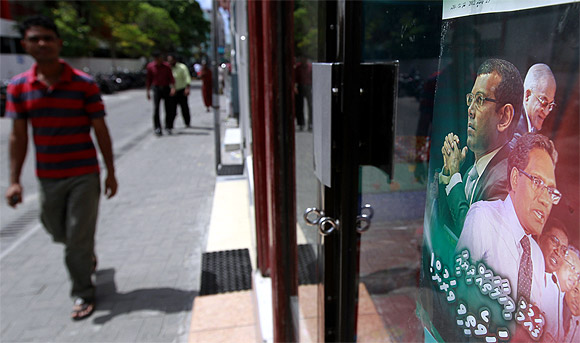 A man walks past a poster which shows former Maldivian presidents Mohamed Nasheed, Abdul Gayoom, and the newly appointed president Mohamed Waheed Hassan Manik