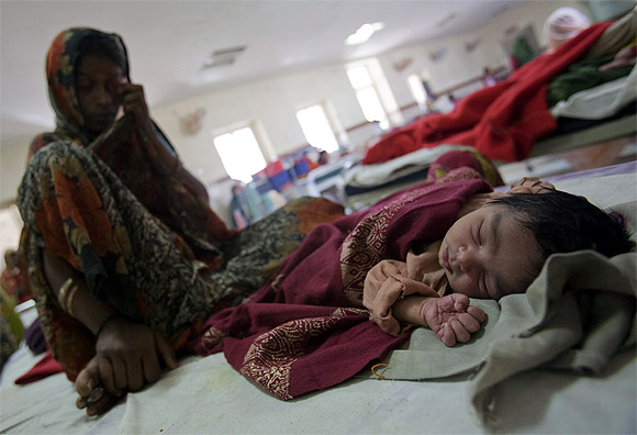 A woman who recently gave birth sits on a bed along with her new born baby