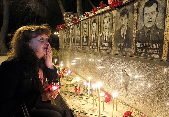 A woman cries in front of a memorial dedicated to firefighters and workers who died after the Chernobyl nuclear disaster during a night service near the Chernobyl plant