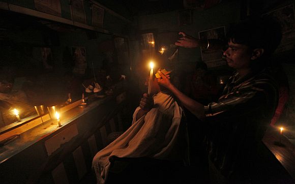 A customer holds a candle as he gets his haircut at a barber's shop during a power-cut in Kolkata