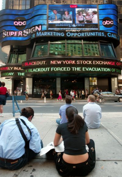 A group of people watch headlines on a board in New York's Times Square August 15, 2003, after the biggest power outage in North American history blacked out New York and other major US and Canadian cities