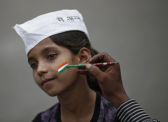 A man paints the tri-colours of India's national flag on the face of a supporter of Hazare in New Delhi