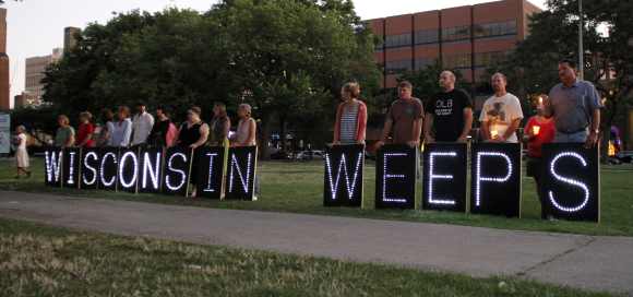 People stand holding a sign expressing their feelings during a vigil at Cathedral Square to honor victims of Oak Creek in downtown Milwaukee, Wisconsin
