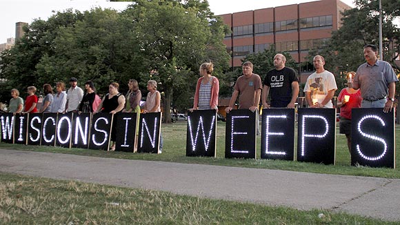 People stand holding a sign expressing their feelings during a vigil at Cathedral Square to honour victims of Oak Creek in downtown Milwaukee, Wisconsin