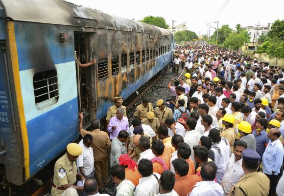 Onlookers stand next to a burnt carriage of the Tamil Nadu Express at Nellore station on July 30. 30 people lost their lives in the mishap
