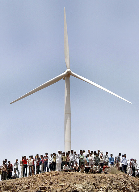 Villagers stand under a power generating windmill turbine at the inauguration of a wind farm at Kalasar, Gujarat