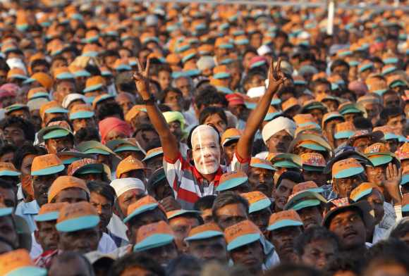 A supporter wears a mask of Modi as he gestures a victory sign during an election campaign rally ahead of the state assembly elections at Pavagadh