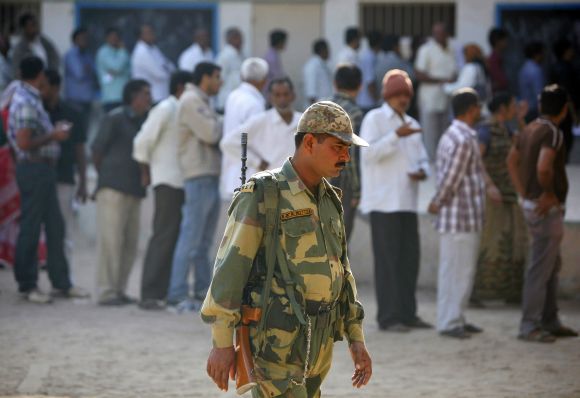 BSF personnel patrols as voters stand in queues to cast their ballots outside polling booths in Gujarat's Sanand