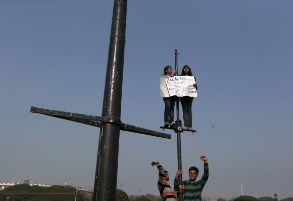 Demonstrators shout slogans and carry a placard while standing on lamp posts during a protest rally near the presidential palace in New Delhi
