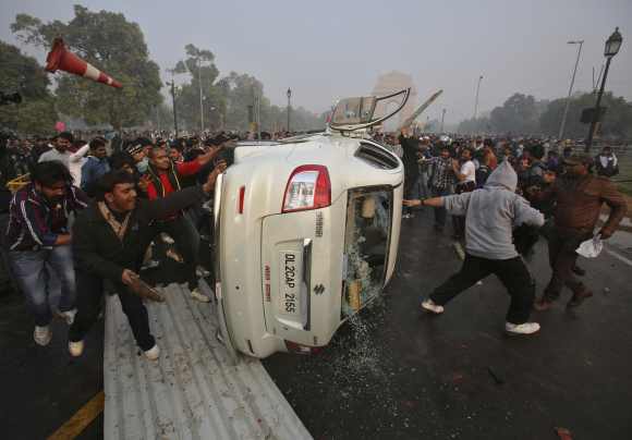 Demonstrators damage a government vehicle after they overturn it in front of the India Gate