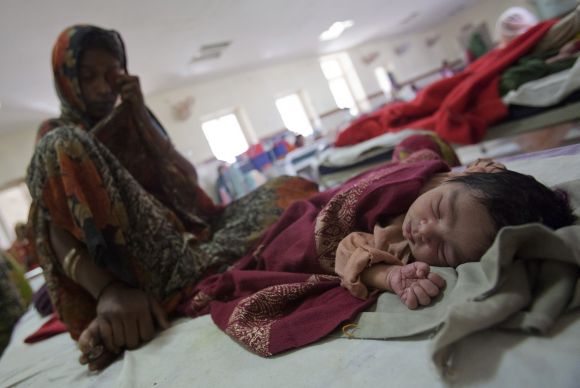 A woman sits on a bed along with her new born baby at a district hospital in Madhya Pradesh.