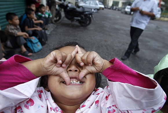 A girl playfully reacts to being photographed while waiting for a school bus in Dharamsala