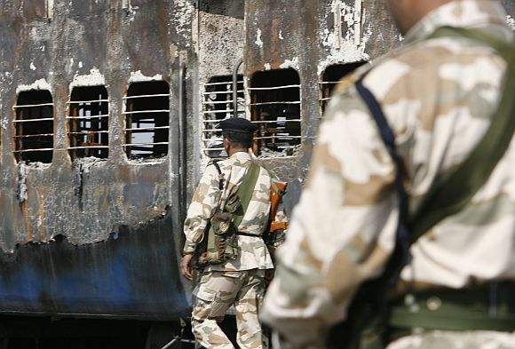 Rapid Action Force personnel stand guard besides a burnt carriage of a Samjhauta Express train in Deewana, near Panipat town, on February 19, 2007. Two bombs exploded aboard the train bound for Pakistan, sparking a fire that killed 68 passengers