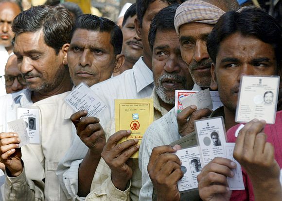 Voters display their election identity cards outside a polling booth in Shahjahanpur, Uttar Pradesh