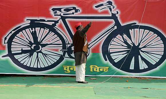 A Samajwadi Party worker gestures in front of a banner with the party's electoral symbol in Allahabad