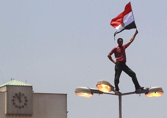 A protester holds an Egyptian flag while standing on a light pole at Tahrir square in Cairo