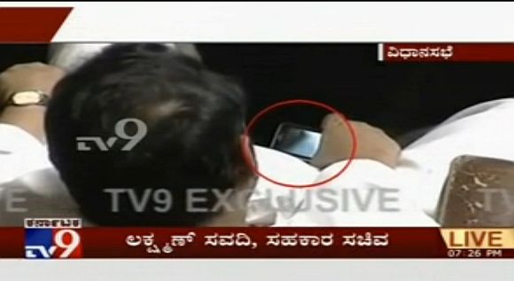 A TV grab of Lakshman Savadi, who held the co-operation portfolio, caught watching a porn clip on a mobile phone