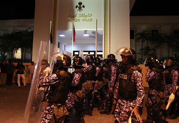 Maldivian police officers walk past the Maldives parliament during a protest, in Male, on Sunday night