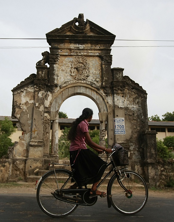 A woman rides a bicycle past a building damaged during the civil war in Jaffna, about 304 km north of Colombo