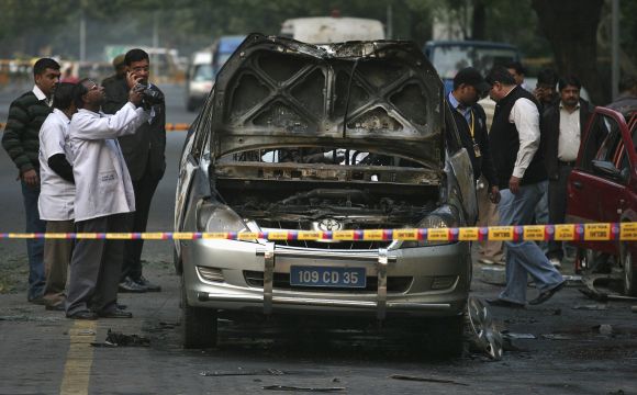 A forensic official takes pictures of a damaged Israeli embassy car after an explosion in New Delhi