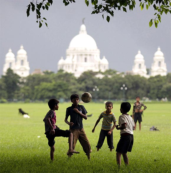 Children play soccer on a field in front of the Victoria Memorial