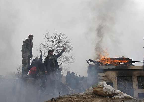 Afghan men shout anti-US slogans near a pile of wood and tyres, set on fire by the protesters, during a protest outside the US military base in Bagram