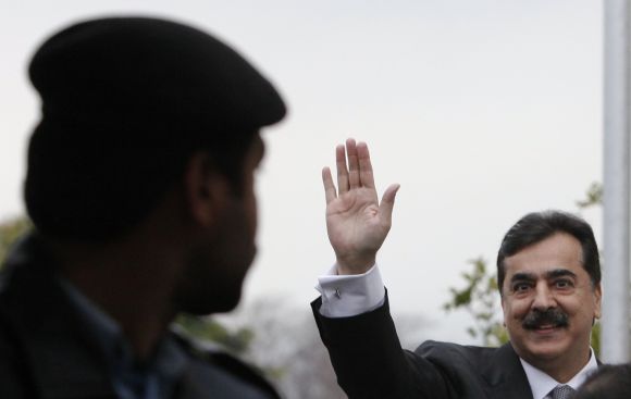 A policeman looks towards Pakistan's Prime Minister Yusuf Raza Gilani waving.