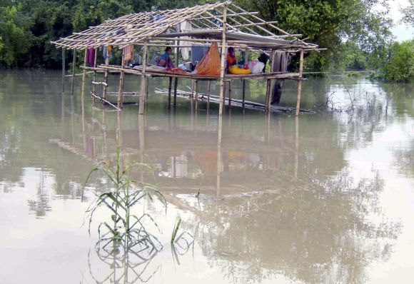 Flood-affected people sit in a damaged hut as they wait for relief supplies after an embankment of river Brahmaputra broke in Arunachal