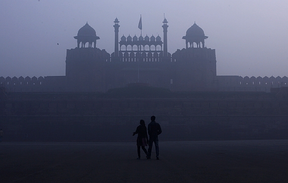 A couple walks in front of the Red Fort amid dense fog on a cold winter morning in the old quarters of Delhi
