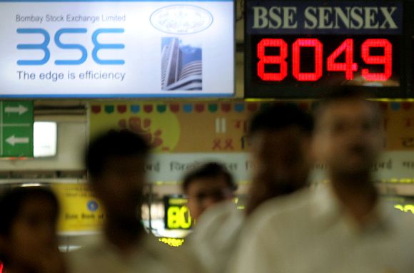 Indian commuters walk past electronic board displaying Bombay Stock Exchange's index at railway station in Mumbai.