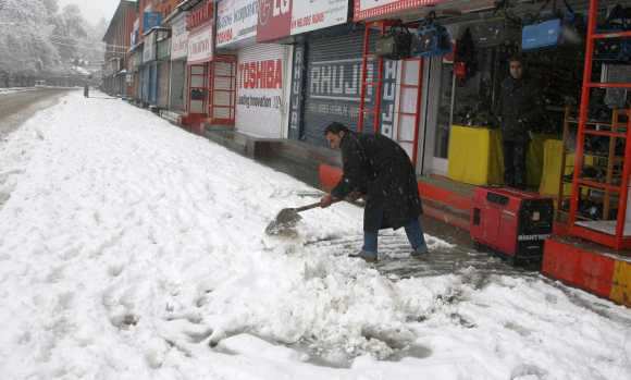 A man clears snow in front of his shop in Srinagar