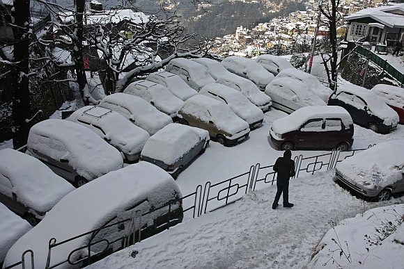 A man walks pasts snow covered cars after heavy snowfall in Shimla.