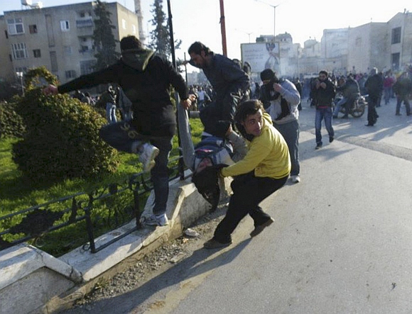Anti-government protesters carry an injured man while covering their faces from tear gas being fired in Adlb