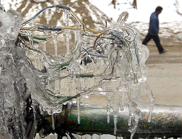 Wires frozen with ice are seen from the first floor of a building as a Kashmiri man walks on a road below in Srinagar