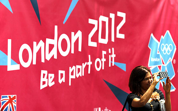 A woman takes a photo in front of a banner showcasing the London 2012 Olympics