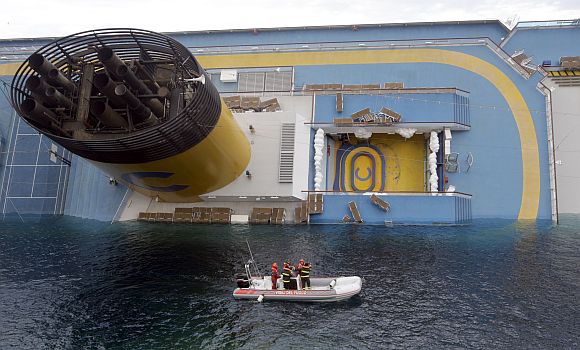 Rescuers stand in a boat next to the Costa Concordia