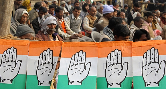 Congress supporters sit next to flags with the party's logo