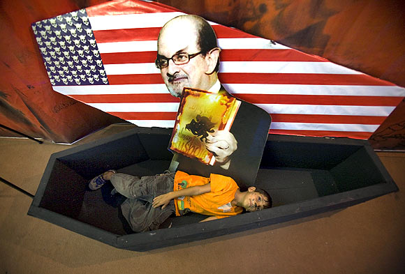 A boy lies in a symbolic coffin for with a picture of author Salman Rushdie