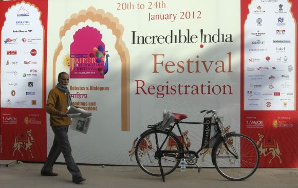 A newspaper vendor walks past an advertisement hoarding outside the venue of the annual Literature Festival in Jaipur