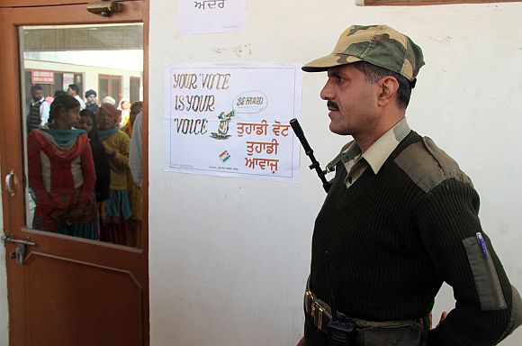 BSF trooper stands guard as voters are reflected in window as they wait to cast their ballots at polling station at Banur, Punjab, on Monday